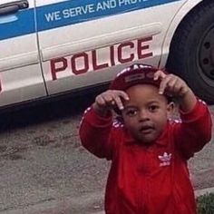 a little boy standing in front of a police car with his hands on his head