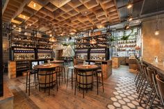 the interior of a restaurant with wooden tables and stools in front of shelves filled with bottles