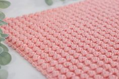 a pink crocheted blanket sitting on top of a white table next to a plant