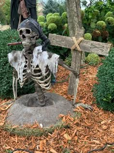 a skeleton sitting on top of a grave next to a wooden cross and shrubbery