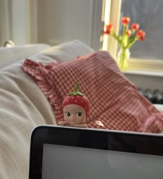 a laptop computer sitting on top of a bed next to a stuffed animal doll with a strawberry on it's head