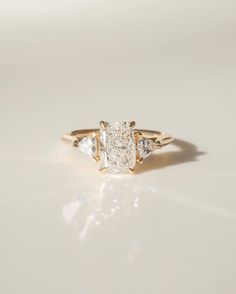 a yellow gold ring with three stones on it, and the center stone is an oval diamond