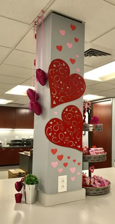 two red hearts are hanging on the side of a tall pillar in an office cubicle