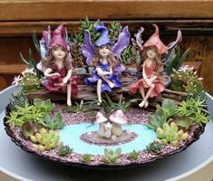 three little fairy figurines sitting on top of a plate with succulents