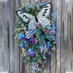 a white butterfly with purple and blue flowers on it's wings hanging from a wooden fence