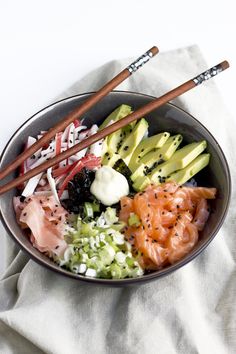 a bowl filled with sushi and vegetables on top of a white cloth next to chopsticks