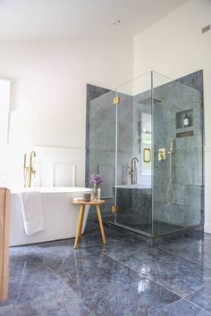 a bathroom with a walk in shower next to a white bath tub and wooden stool