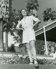 an old black and white photo of a woman standing in front of a building with her hands on her hips