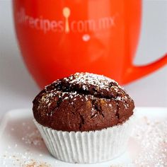 a chocolate muffin sitting on top of a white plate next to a red mug