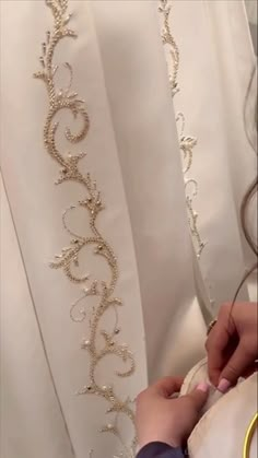 a woman is working on the back of a white dress with gold sequins