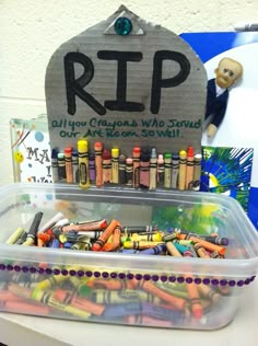 a plastic container filled with crayons sitting on top of a table next to a sign