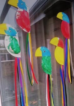 paper plate birds and parrots are hanging from the window sill with streamers