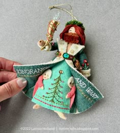 a hand holding an ornament that is shaped like a christmas tree girl with red hair and green dress