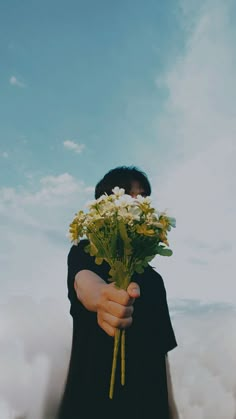 a person holding flowers in their hands with clouds and blue sky behind them on a sunny day