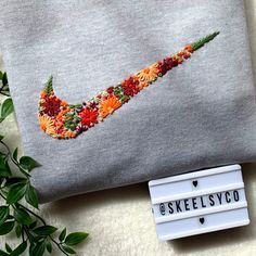 a grey sweatshirt with an orange and red flowered nike logo on it next to a plant