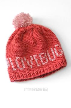 a red knitted hat with white letters and a pink pom - pom