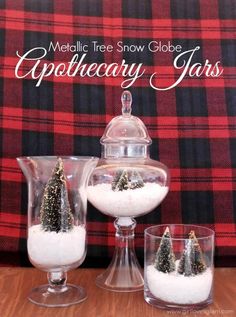 three glass vases filled with snow and trees on top of a wooden table next to a plaid blanket