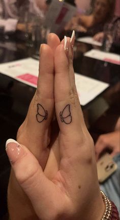 two people holding hands with small tattoos on their fingers and the other hand is in the air