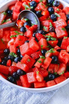 a bowl filled with watermelon, blueberries and strawberries next to a spoon