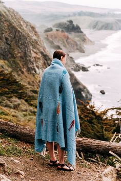 a woman standing on top of a hill next to the ocean wearing a blue ponchy