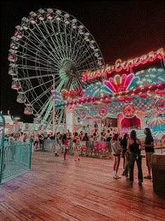 people are standing around in front of a ferris wheel at the fairground with lights on