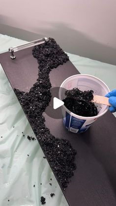 a person in blue gloves is holding a paintbrush and mixing black soil into a bucket