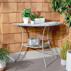 two potted plants sitting on top of a metal table next to a brick wall