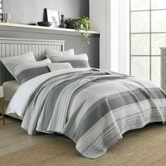 a bed in a bedroom with grey and white striped comforter on top of it