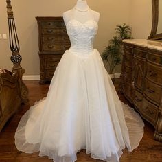 a wedding dress is displayed on a mannequin in front of a dresser and mirror