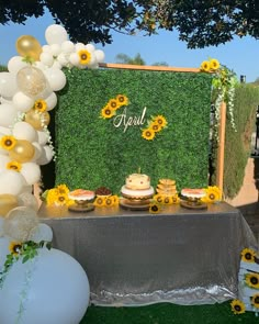 a table with sunflowers and cake on it in front of a green backdrop