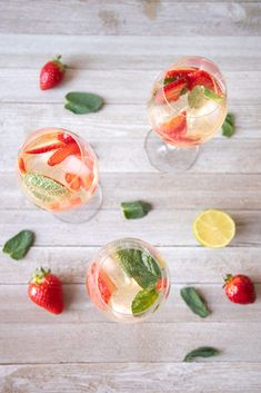 three glasses filled with fruit and ice on top of a wooden table next to sliced strawberries