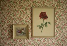 two framed pictures hang on the wall next to a flowered wallpaper with pink and red flowers