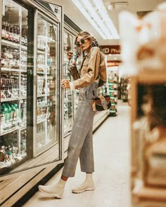 a woman standing in front of a glass case filled with drinks and sodas at a grocery store