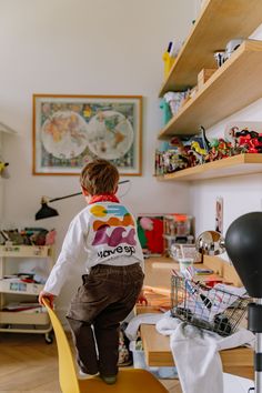 a young boy sitting on top of a yellow chair next to a wooden shelf filled with toys