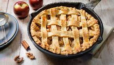 an apple pie sitting on top of a wooden table next to some nuts and apples