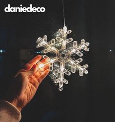 a hand is holding an illuminated snowflake ornament