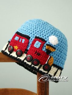 a crocheted hat with a train on it sitting on top of a wooden chair