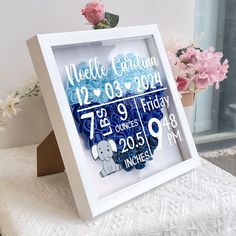 a white frame holding a baby's birth date and flowers on a table next to a vase with pink roses