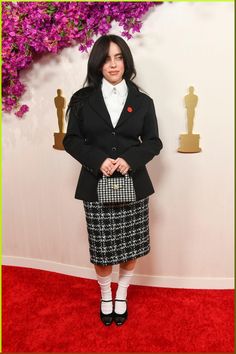 a woman standing on a red carpet wearing a skirt and jacket