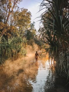 a person wading in a river with steam rising from the water and trees around