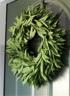 a wreath hanging on the front door of a house with green leaves and branches around it