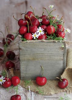 a wooden box filled with cherries and daisies on top of burlocks