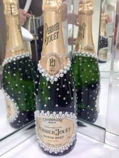 three bottles of champagne are on display in front of a glass case that is filled with pearls