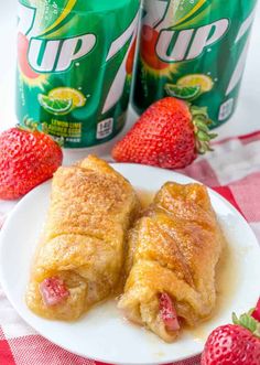 two pastries on a white plate with strawberries next to cans of up 7up