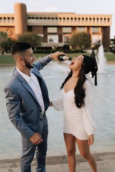 a man and woman standing next to each other in front of a fountain drinking wine