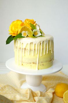 a yellow cake with white icing and flowers sitting on a table next to sliced lemons