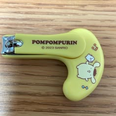 a pair of yellow scissors sitting on top of a wooden table with the words pompompurin printed on it