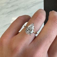 a woman's hand with a diamond ring on top of her finger, next to a white marble countertop