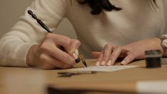 a woman sitting at a table writing with a pen and paper in front of her