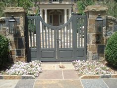 an entrance to a home with stone walls and gated in plants on either side